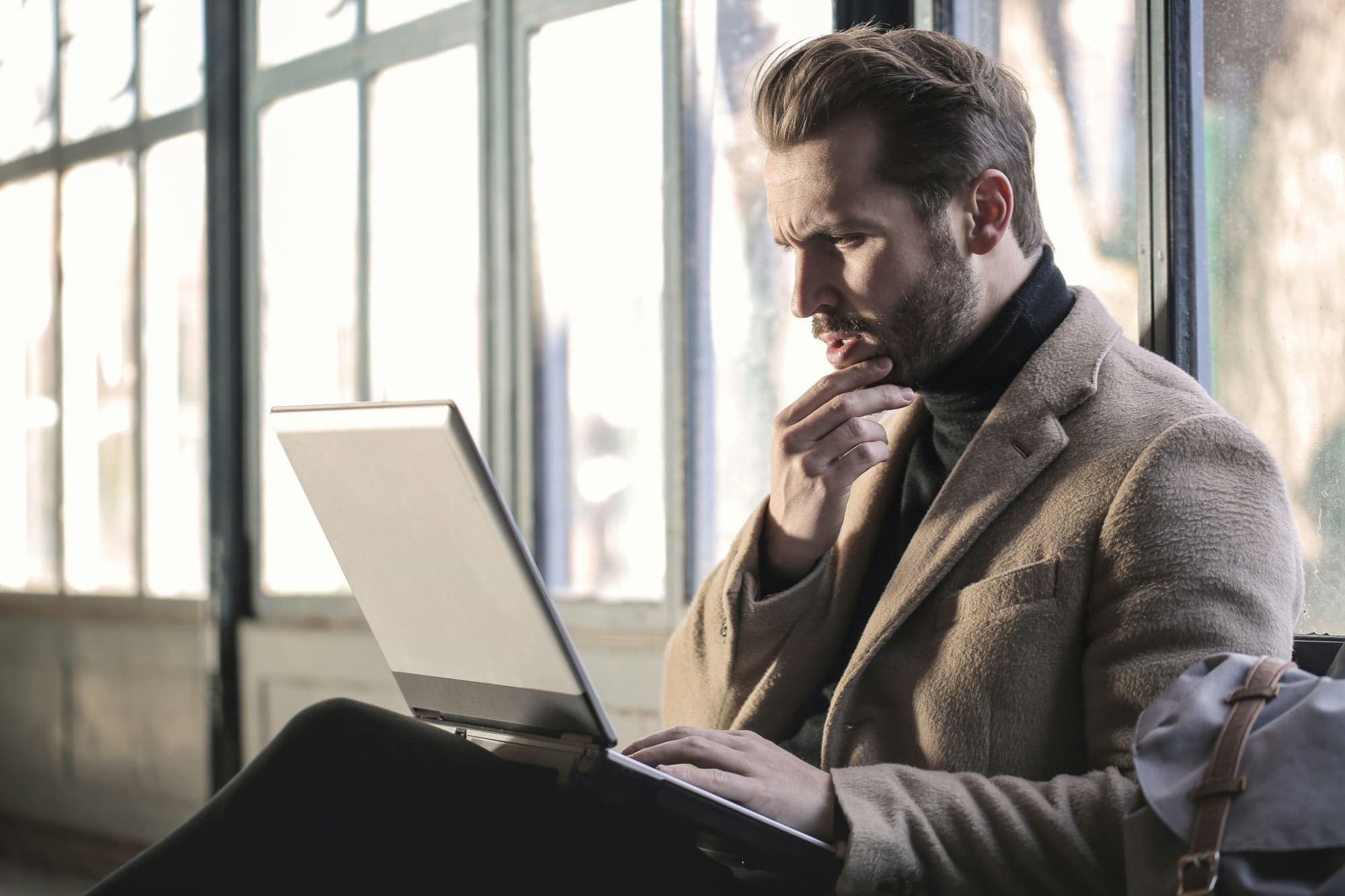 窓辺でノートPCに向かい思考する男性