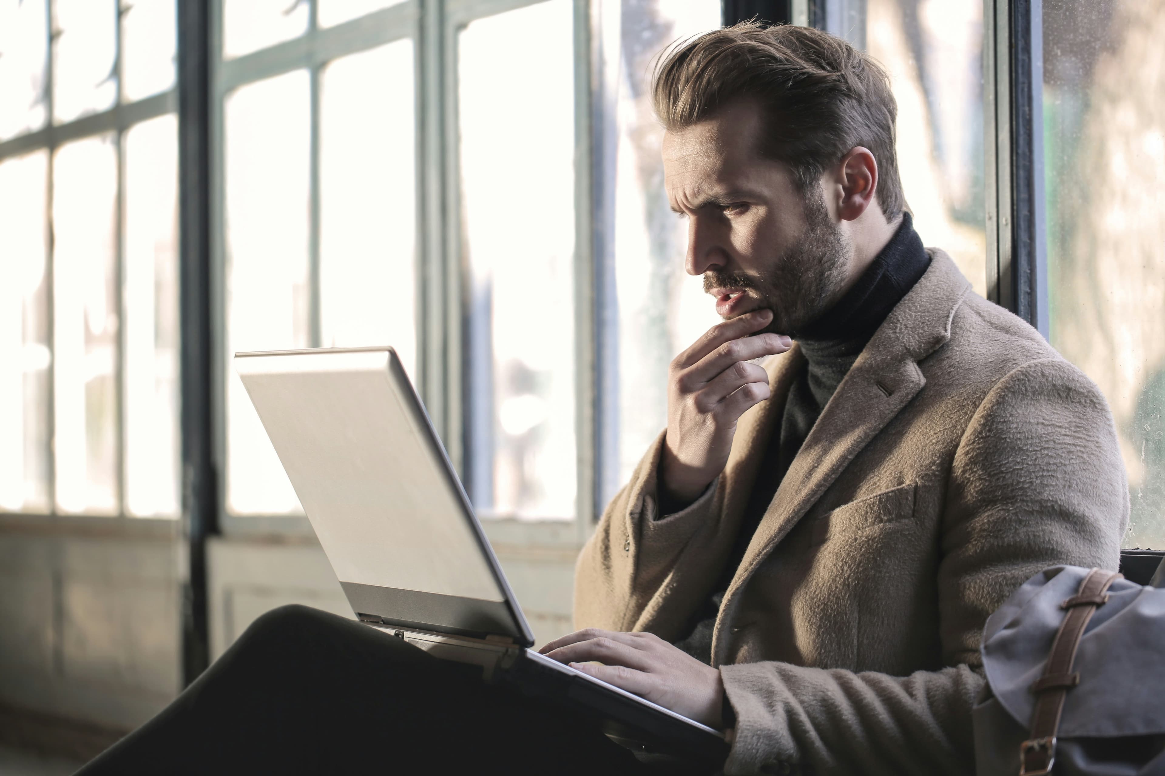 窓辺でノートPCに向かい思考する男性